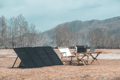 Portable solar power setup on dry grass with EcoFlow solar panels, outdoor camping gear, and a mountain landscape in the background. Perfect for off-grid renewable energy solutions and outdoor adventures.